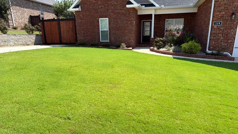 Green bermuda lawn in front of a brick house with landscaped flower beds and walkway