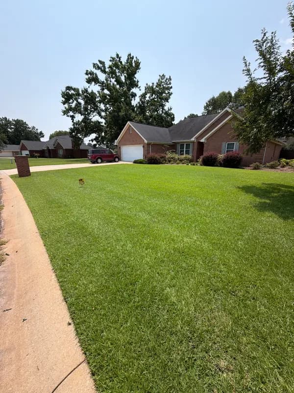 Lush green lawn in front of a brick ranch home with a red minivan in the driveway