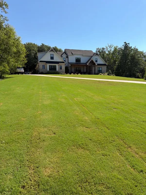 Two-story home with brick and board-and-batten siding behind a mowed green lawn under blue sky