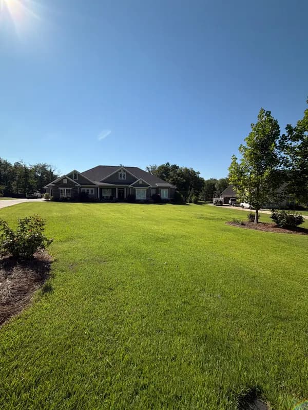 Wide shot of lush green lawn leading up to a large brick and siding home under a clear blue sky