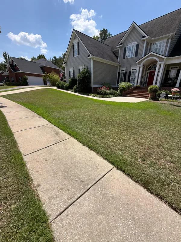 Two-story gray house with landscaped beds and a green front lawn along a concrete walkway