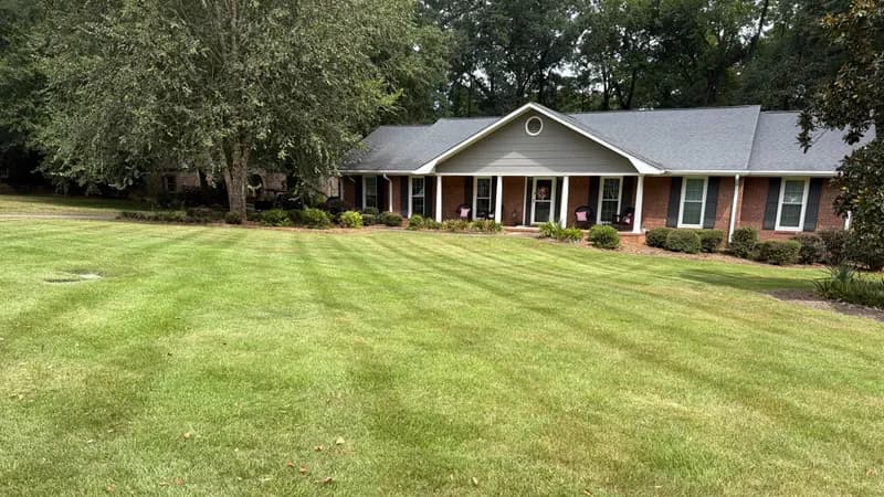Well-manicured green lawn with mow stripes in front of a single-story brick house