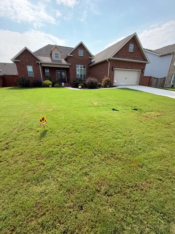 Two-story brick home with a green bermuda lawn and a yellow lawn care service sign in the front yard