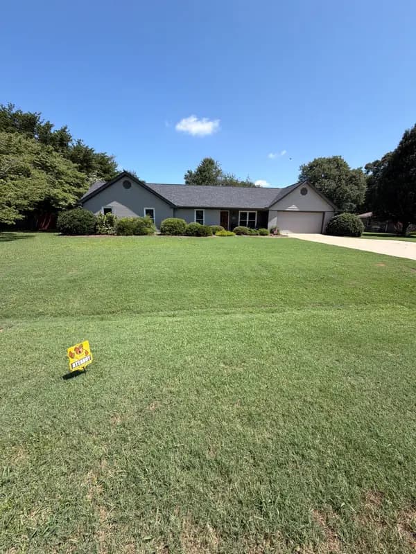 Ranch-style home with green lawn and lawn care company yard sign on a sunny day