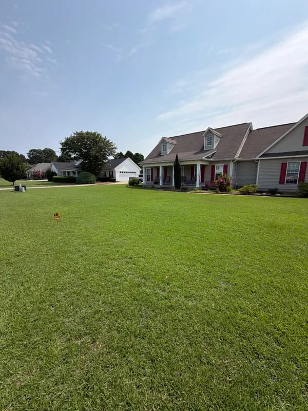 Wide green lawn in front of a two-story house with red shutters under a blue sky