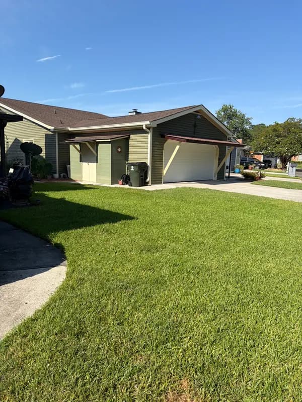 Green, well-maintained lawn in front of a house with an attached garage and storage shed under blue sky