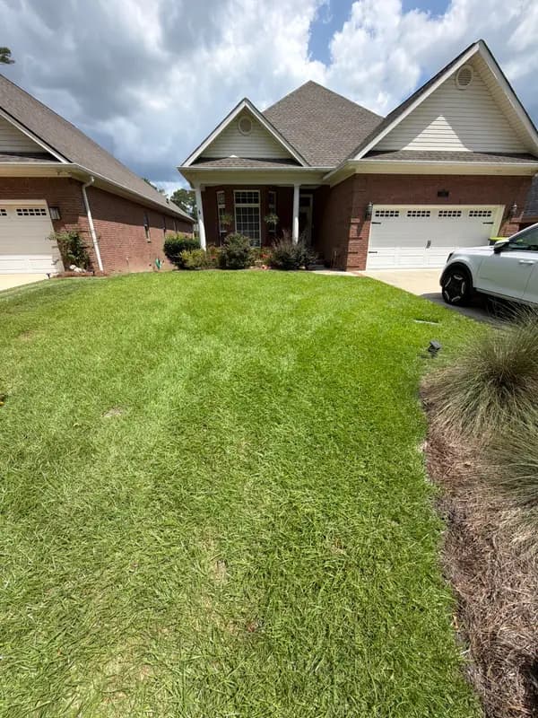 Green front lawn with mowing stripes leading up to a brick house with white garage doors