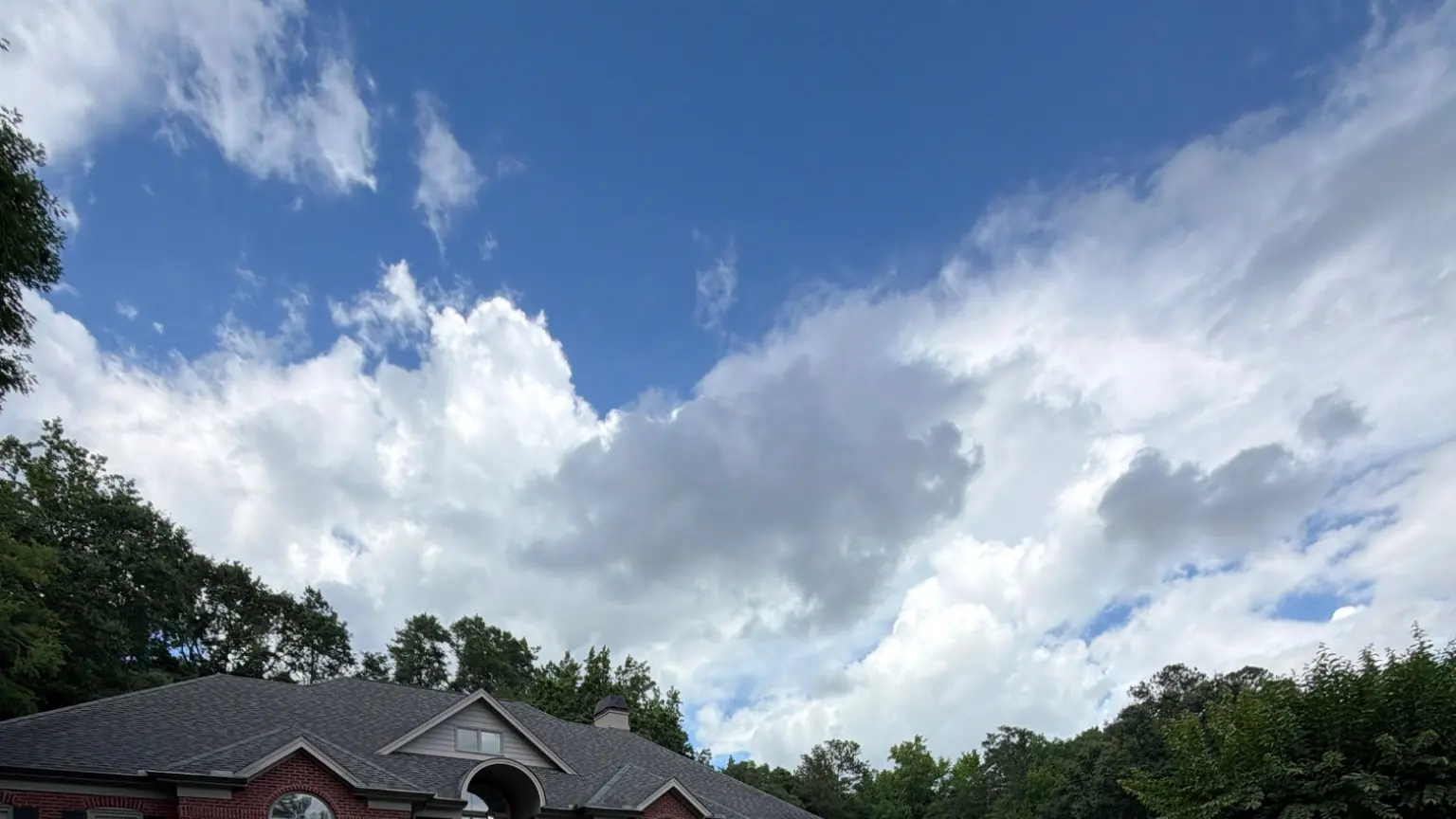 Green lawn sloping up to a brick home with a lawn care sign, under a partly cloudy sky