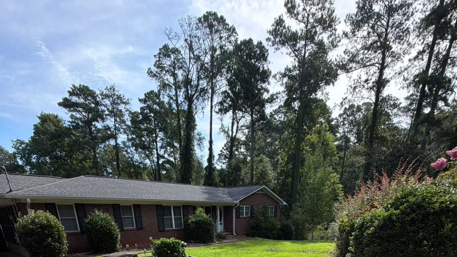 Brick ranch home with green lawn, mulched flower beds, and tall pine trees in background