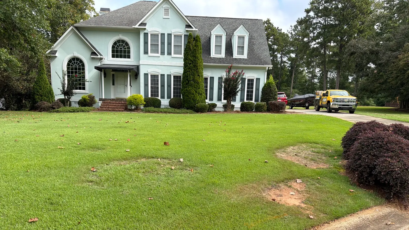 Lush green lawn with scattered fallen leaves in front of a two-story light blue house