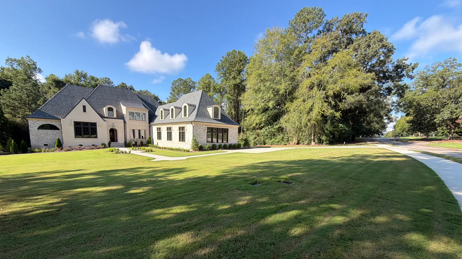 Large stone home with dormer windows behind a wide, freshly mowed green lawn and mature trees